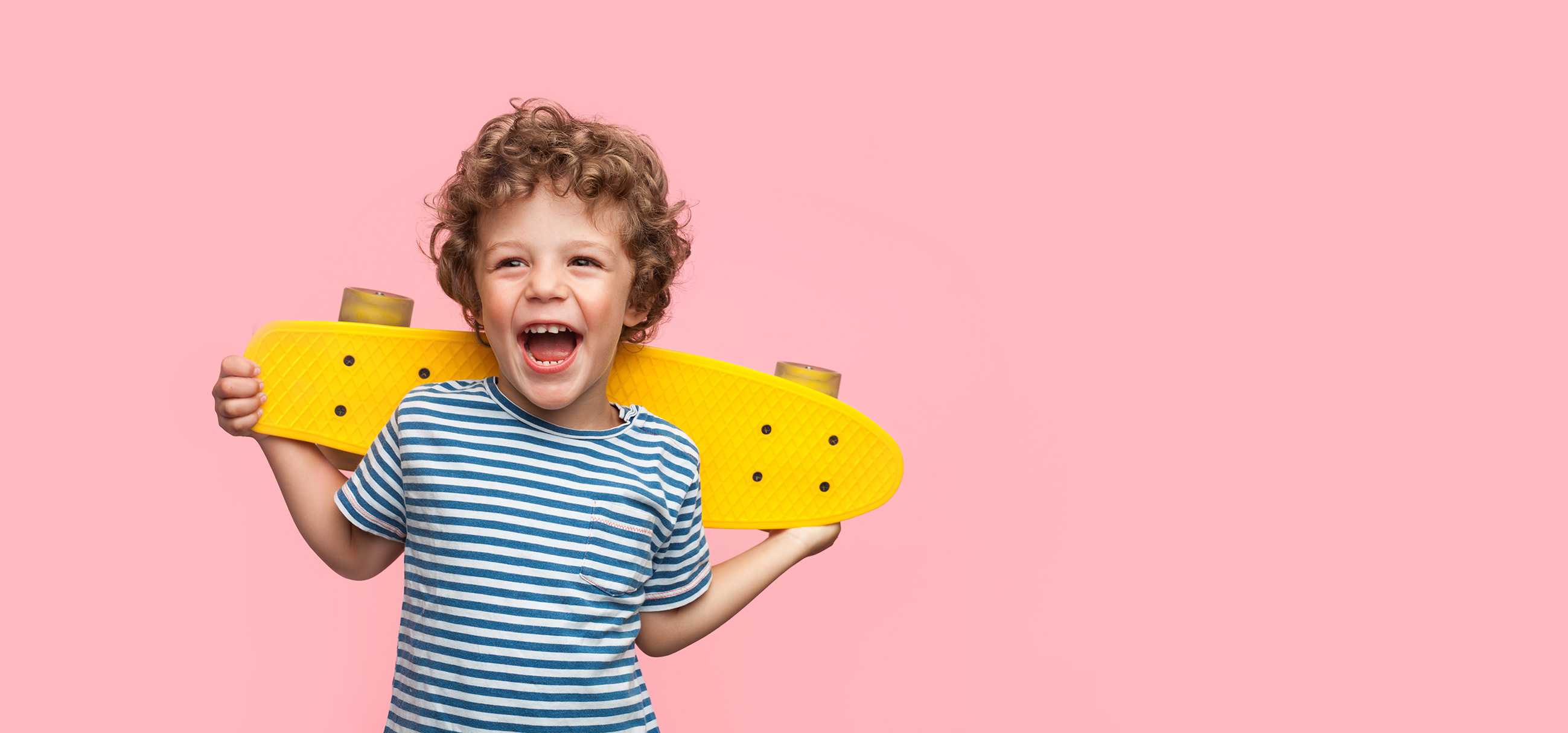 Niño sonriendo con un patinete amarillo sobre fondo rosa