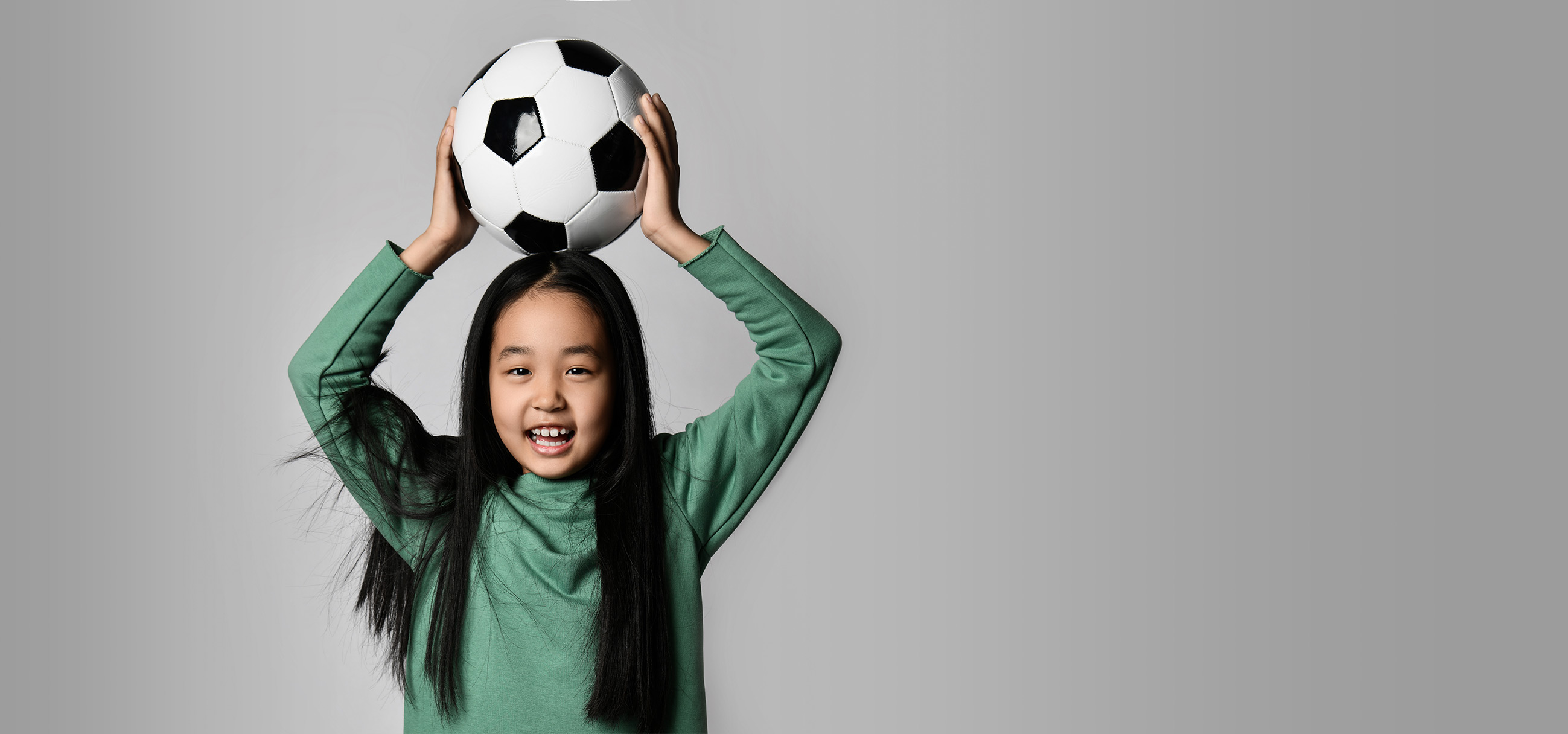 Niña con un balón de fútbol sobre fondo gris